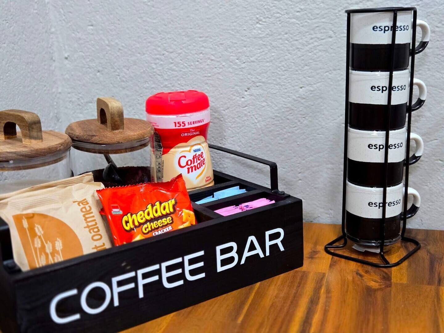 Un coin café aménagé avec une machine à café, un pot de crème à café, un paquet de crackers au fromage cheddar et un porte-tasses étiqueté « espresso ».