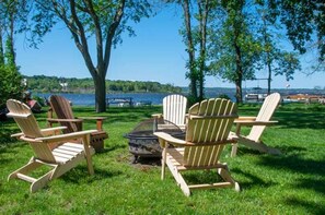 A lakeside setting with Adirondack chairs arranged around a fire pit. - Ducking Away Cottage (Tay)