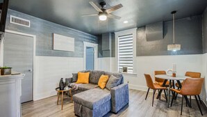 A modern living room with a gray sofa, orange cushions, a coffee table, and a dining area with a round table and chairs. - Sunset Sanctuary - El Paso (El Paso)