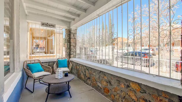 A balcony with wicker furniture, a stone wall, and a view of the street. - Sunset Sanctuary - El Paso (El Paso)