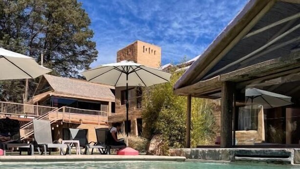 A pool area with lounge chairs and umbrellas, a stone building with a tower, and a clear blue sky. - Vientonorte (Tilcara)