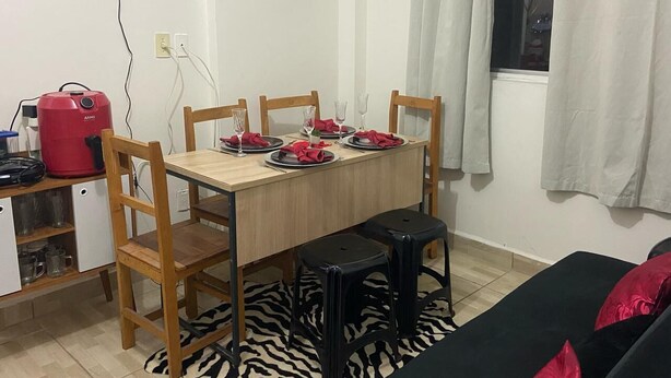 Un comedor con una mesa de madera dispuesta para cuatro personas, cuatro sillas de madera, dos taburetes negros y un electrodoméstico rojo a la izquierda.