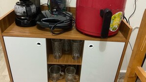 Una kitchenette con cafetera, una freidora de aire roja y un molinillo de café sobre un mueble de madera.