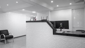 Un área de recepción moderna con mostrador, una silla de oficina negra, un televisor de pantalla plana y una ventana con persianas.