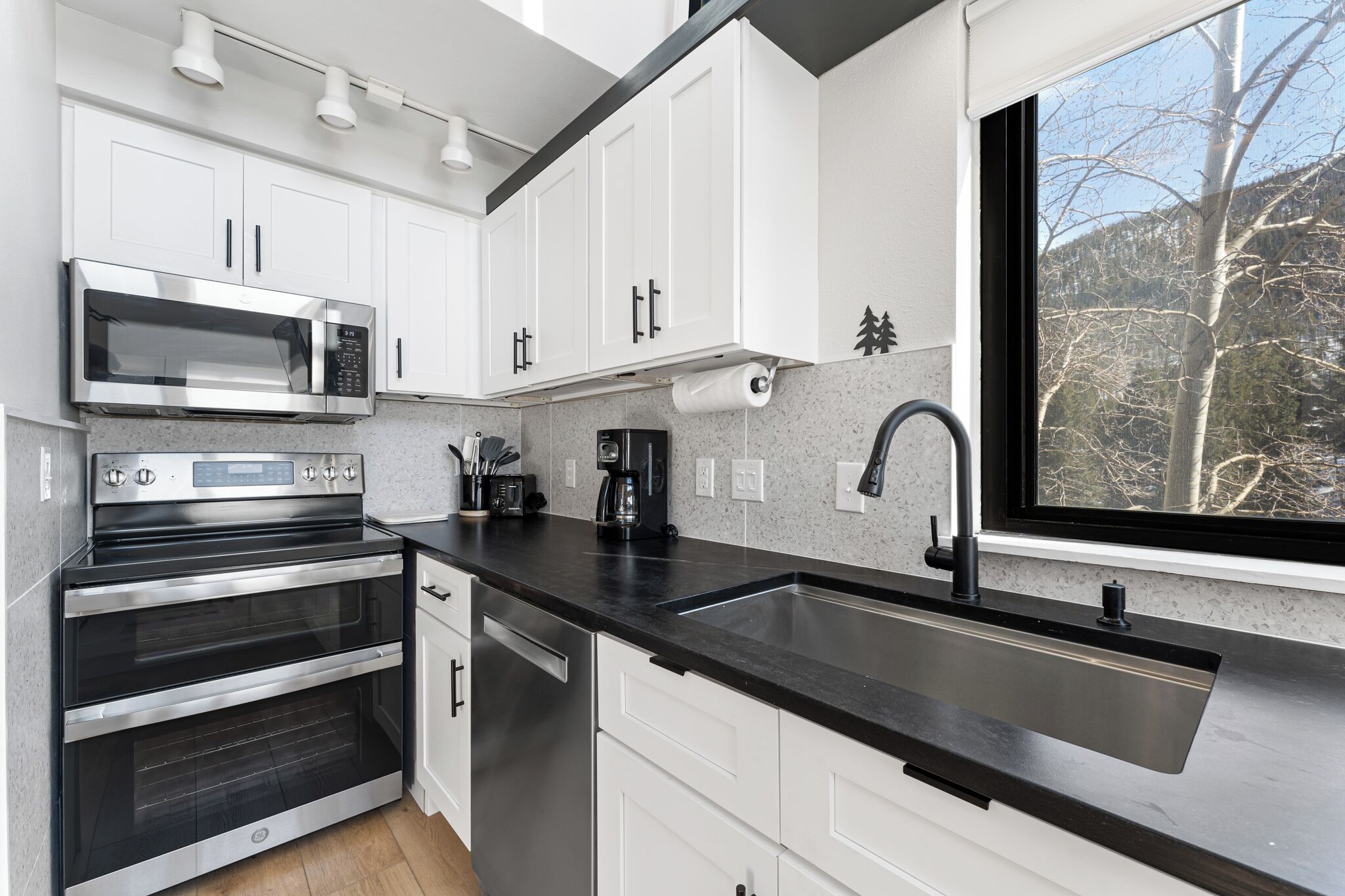 Een moderne keuken met roestvrijstalen apparatuur, witte kasten en een zwart aanrecht.