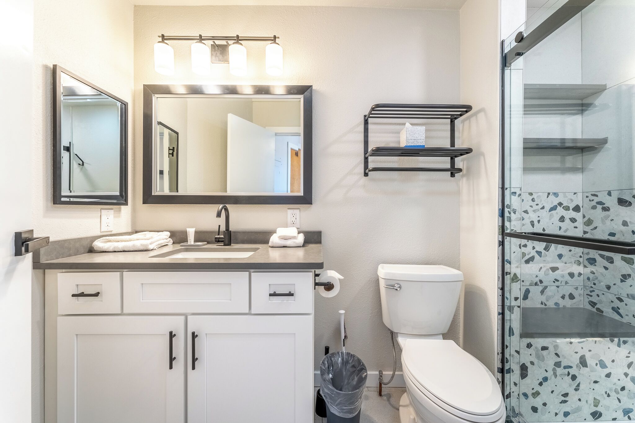 A modern bathroom with a sink, mirror, and toilet. There is a towel rack above the sink and a trash can next to the toilet.