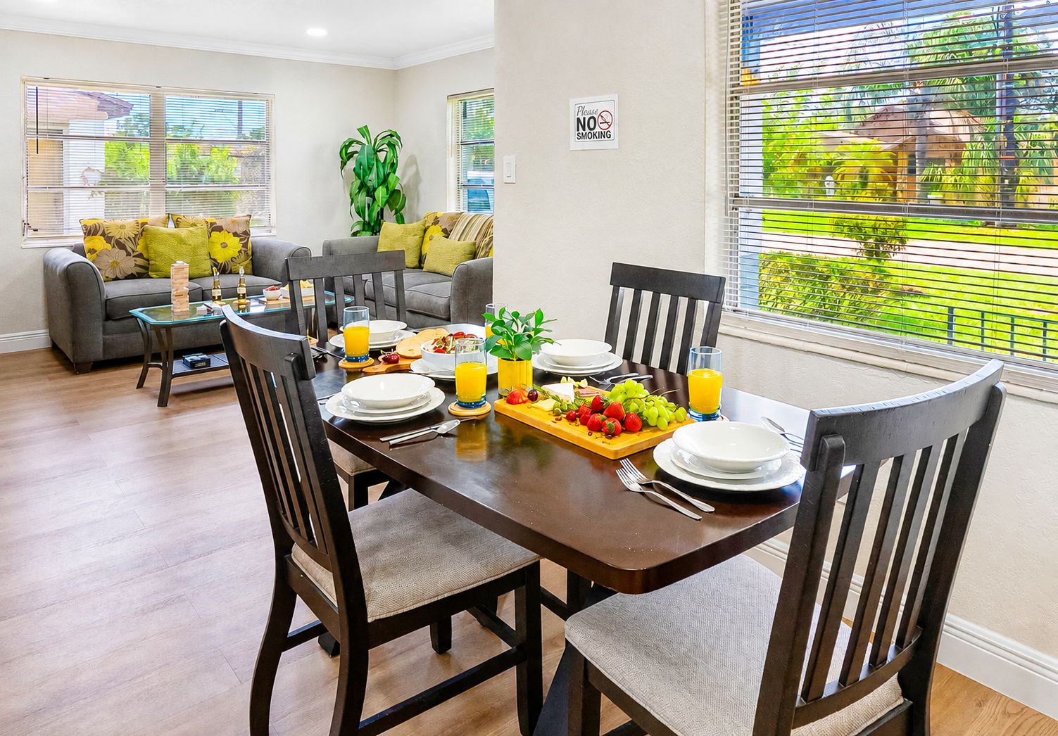 A dining area with a wooden table set for breakfast, surrounded by chairs, with a view of greenery outside.