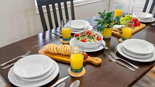 Una mesa de comedor preparada con platos, cubiertos, ensalada, fruta y jugo.