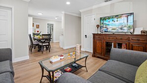 Una sala de estar con una mesa de centro de vidrio, sofás grises, un aparador de madera y un televisor que muestra una escena de playa.