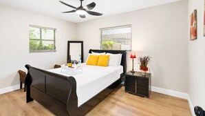 A modern bedroom with a bed, bedside table, nightstand, and ceiling fan.