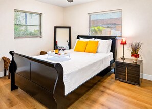A hotel room with a wooden bed, a bedside table with a lamp, and a window with blinds.