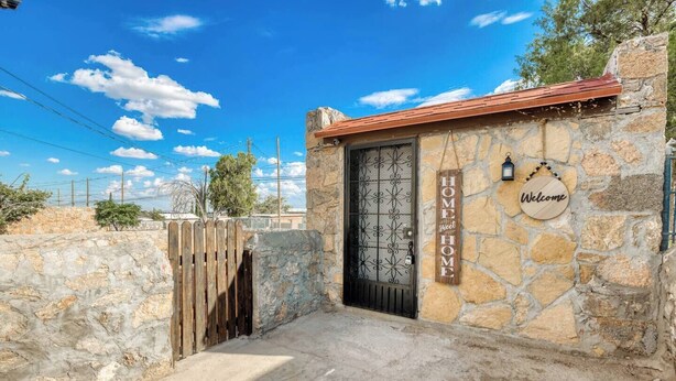 A stone house with a metal gate, a wooden sign reading "HOME sweet HOME", and a "Welcome" sign on the wall.
