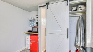 A compact kitchen with a sliding door closet, a microwave, a red refrigerator, and a small countertop with a kettle and coffee maker.