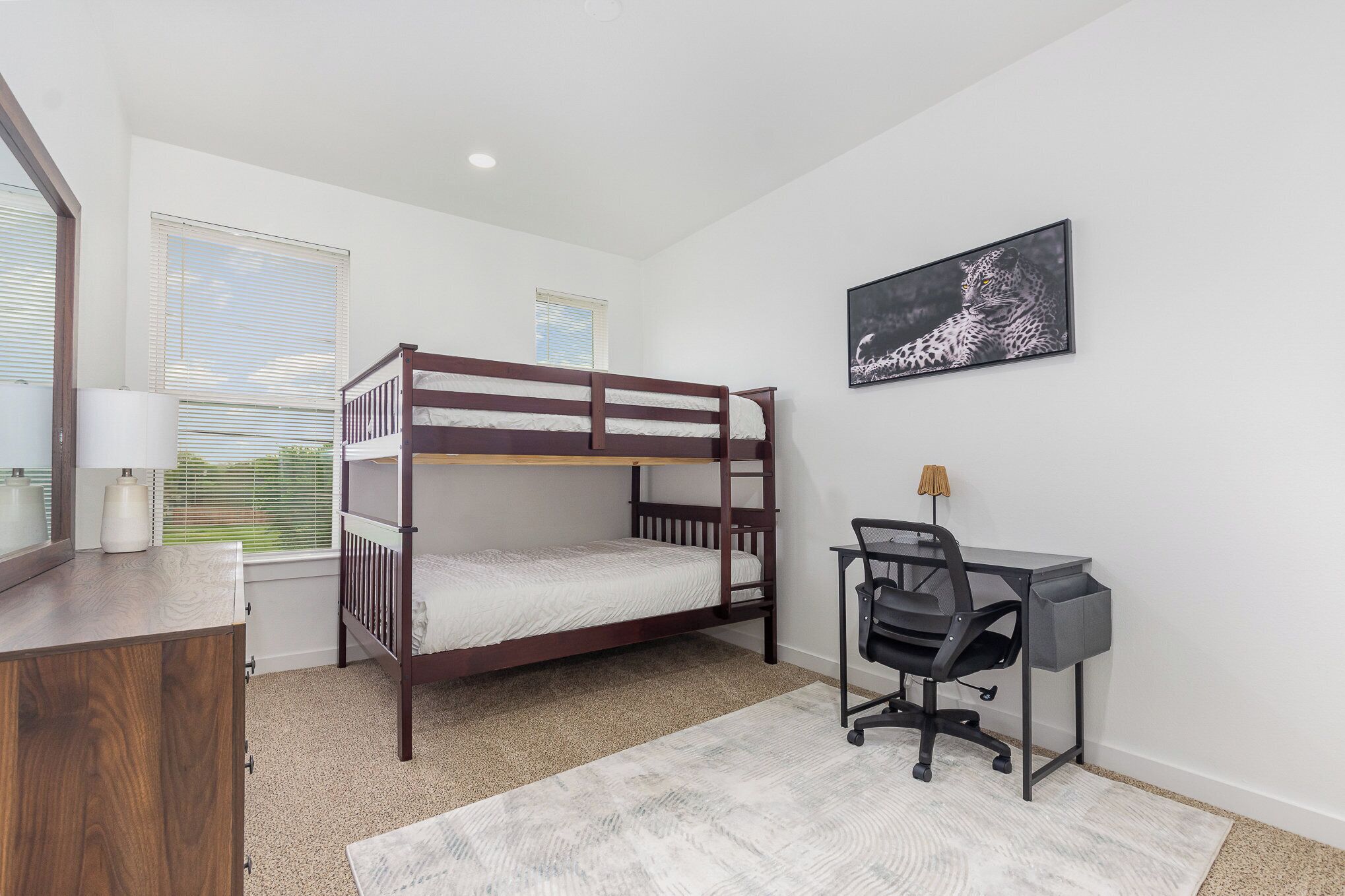 A bedroom with a bunk bed, a desk with a chair, a lamp, and a framed picture on the wall.