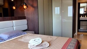 Ein modernes Schlafzimmer mit einem großen Bett, einem Kopfteil, einem Kleiderschrank und einem durch eine Glastür einsehbaren Badezimmer.