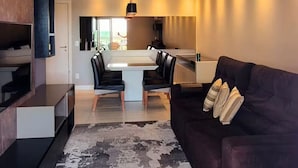 Ein modernes Wohnzimmer mit einem dunkelbraunen Sofa, einem gemusterten Teppich und einem Essbereich mit einem weißen Tisch und Stühlen.