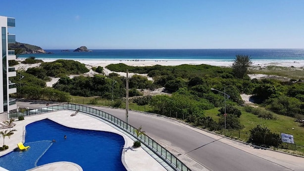 Ein Pool mit geschwungener Kante, eine Straße und ein Strand mit Personen in der Ferne.