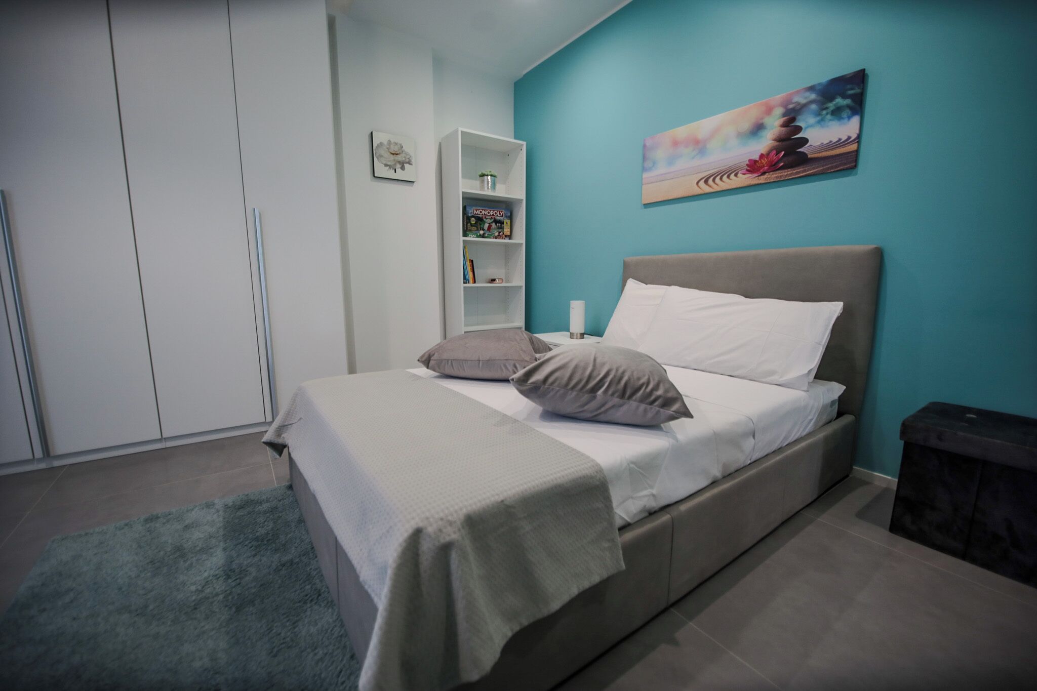 A bedroom with a bed, a bookshelf, and a painting on the wall.
