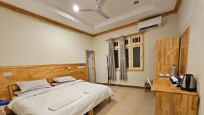 A hotel room with a wooden bed, a desk with a kettle, and a ceiling fan. - Kuri Himandhoo Inn (Himandhoo)
