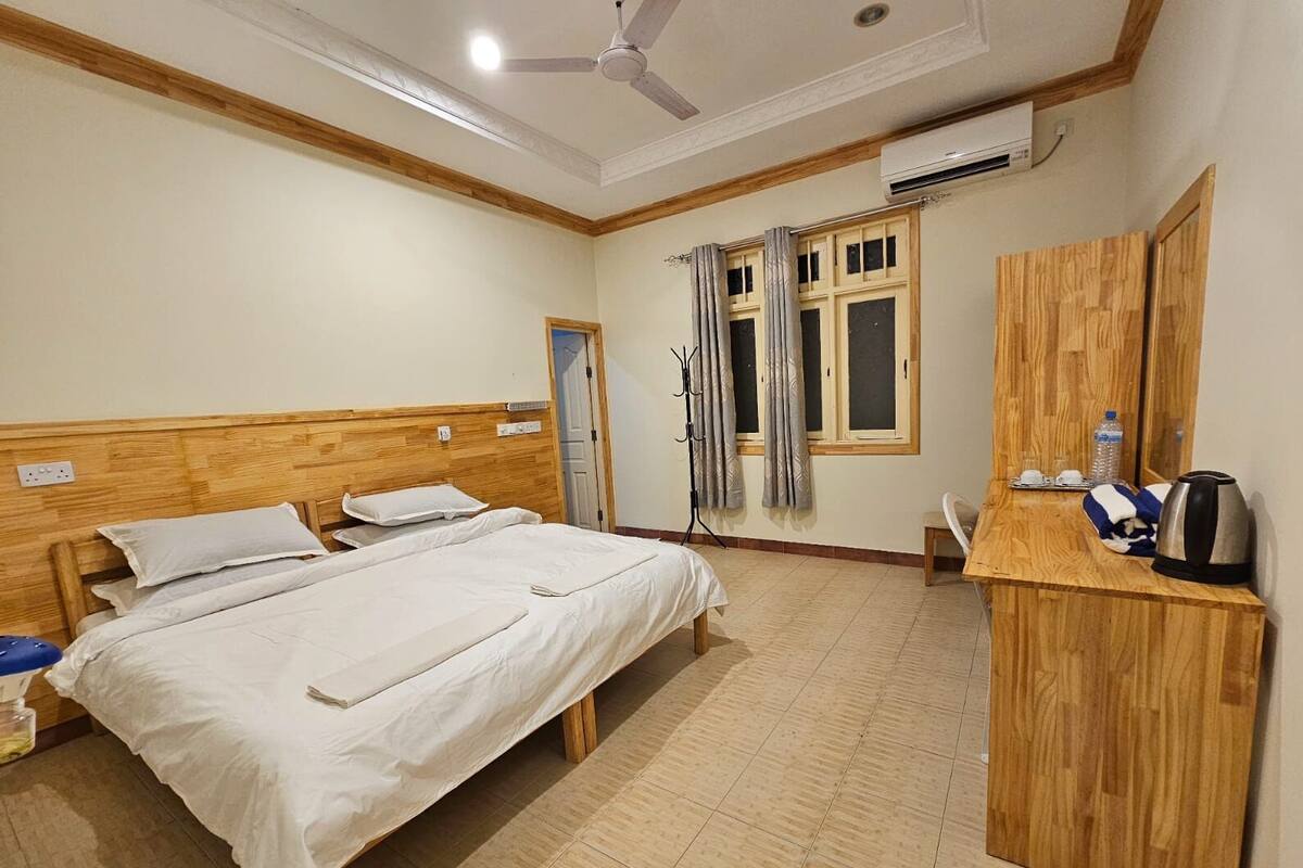 Una habitación de hotel con una cama de madera, un escritorio con hervidor y un ventilador de techo.