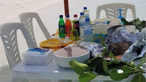 A beachside table with plastic chairs, a table umbrella, bottled drinks, and food items. - Kuri Himandhoo Inn (Himandhoo)