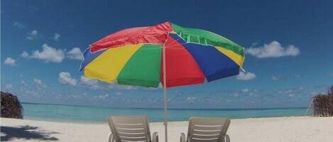 A beach with two lounge chairs under a multicolored umbrella.