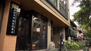 Un immeuble avec une grande entrée en verre, une enseigne indiquant « APPARTEMENTS ROSANEGRA », et une personne qui marche devant.