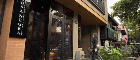 A building with a large glass entrance, a sign reading "ROSANEGRA APARTMENTS," and a person walking in front.