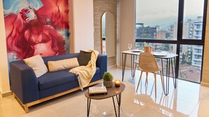 Un salon moderne avec un canapé bleu, une petite table ronde et une grande fenêtre donnant sur la ville.