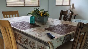 A dining area with a table covered by a patterned tablecloth, wooden chairs, a flower vase, and a remote control on the table. - Baja Escape ;Work, Leisure or Explore — Your Choice! (Loreto)
