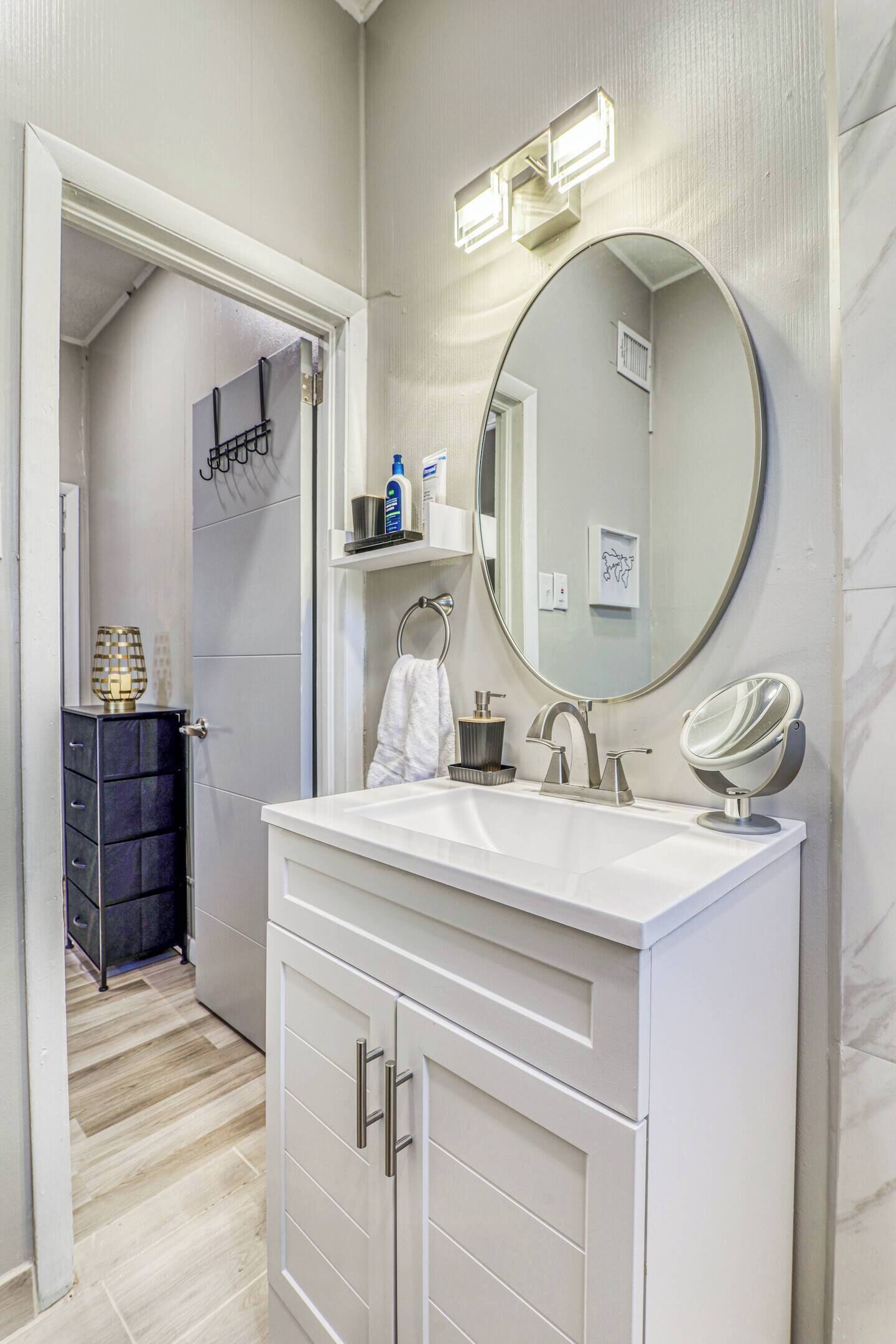 A modern bathroom with a white vanity, a large mirror, and a lighted vanity mirror.