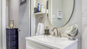 A modern bathroom with a white vanity, a large mirror, and a lighted vanity mirror.