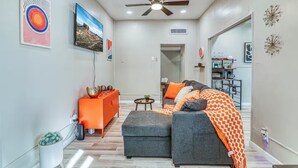 Uma sala de estar moderna com um sofá cinzento, detalhes em laranja e obras de arte nas paredes.