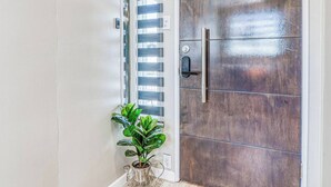 Um corredor com piso de madeira, um vaso com planta e uma porta com puxador metálico.