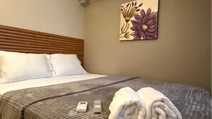 A neatly made bed with white pillows, a gray textured bedspread, and two rolled towels on the bed.