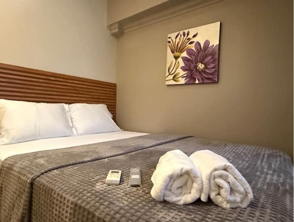 A neatly made bed with white pillows, a gray textured bedspread, and two rolled towels on the bed. - Lovely Studio Apartment in Zona Bancaria (Panamá)