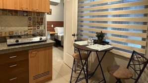 A compact kitchen with wooden cabinets, a gas stove, and a small dining area with two stools.
