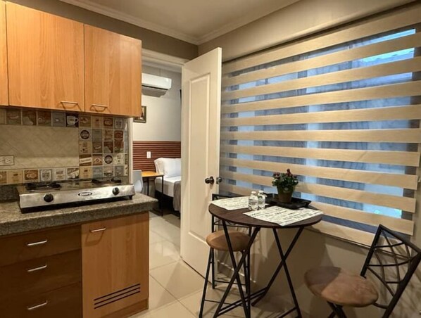 Una cocina compacta con muebles de madera, estufa a gas y un pequeño comedor con dos taburetes.