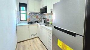 A compact kitchen with white cabinets, a stainless steel refrigerator, and a tiled backsplash.