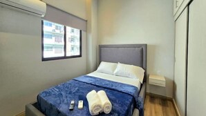 A modern hotel room with a bed, a window, an air conditioner, and a wardrobe.