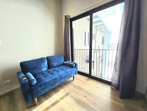 A blue sofa in a room with a wooden floor and a sliding glass door leading to a balcony.