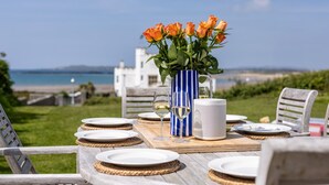 Ein gedeckter Tisch mit Meerblick, eine Vase mit orangefarbenen Rosen und eine weiße Karaffe.