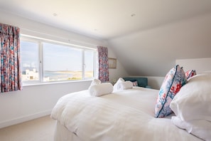 Een hotelkamer met een groot bed, twee opgerolde handdoeken, bloemen gordijnen en uitzicht op zee.