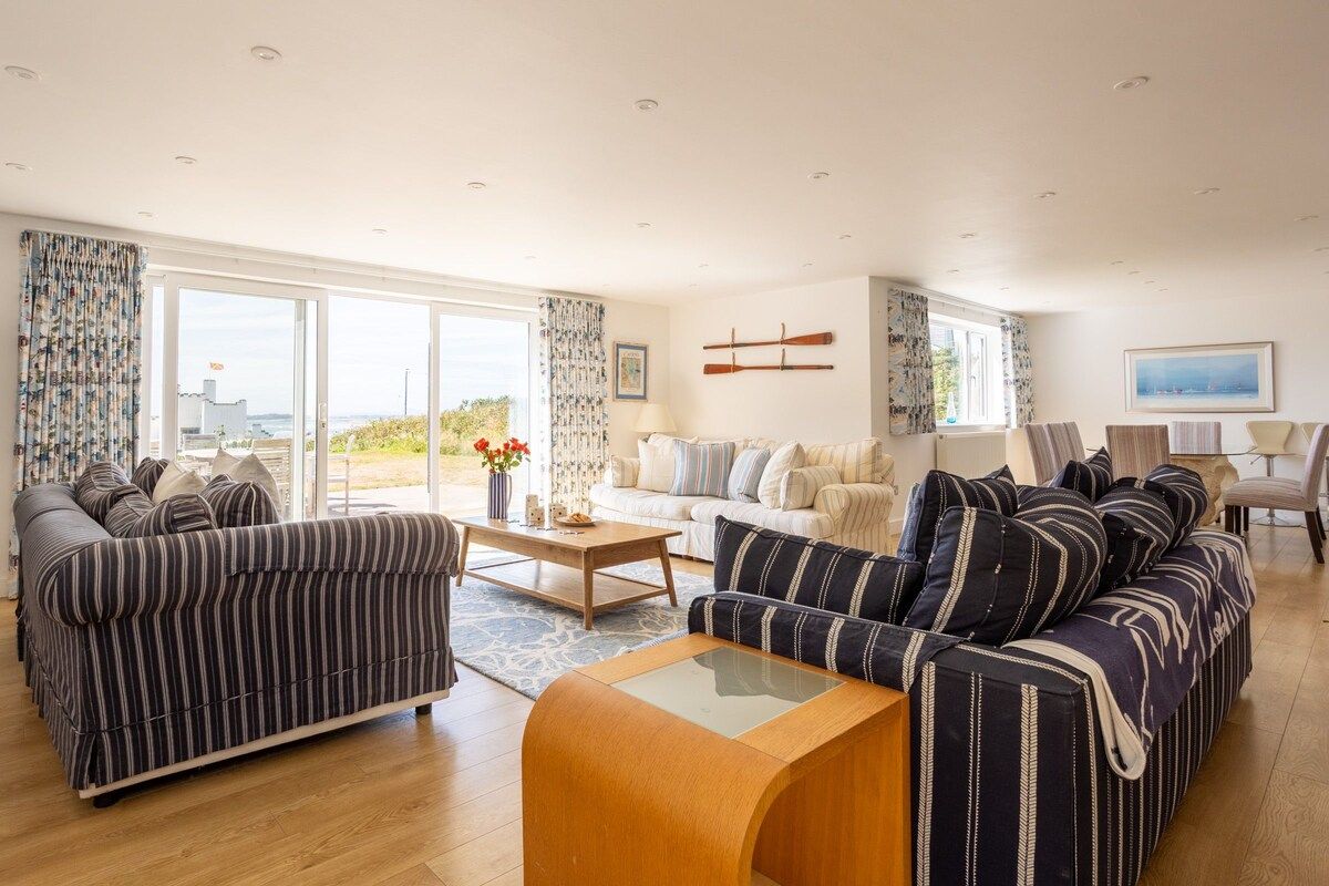 A spacious living room with a striped sofa set, a coffee table, and a view of the outdoors through large windows.