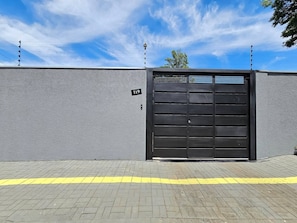 A grey building with a black gate, a yellow line on the pavement, and a clear sky.