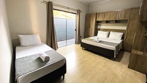 Una habitación de hotel con dos camas, una puerta corrediza de vidrio, un armario de madera y una mesita de noche pequeña.