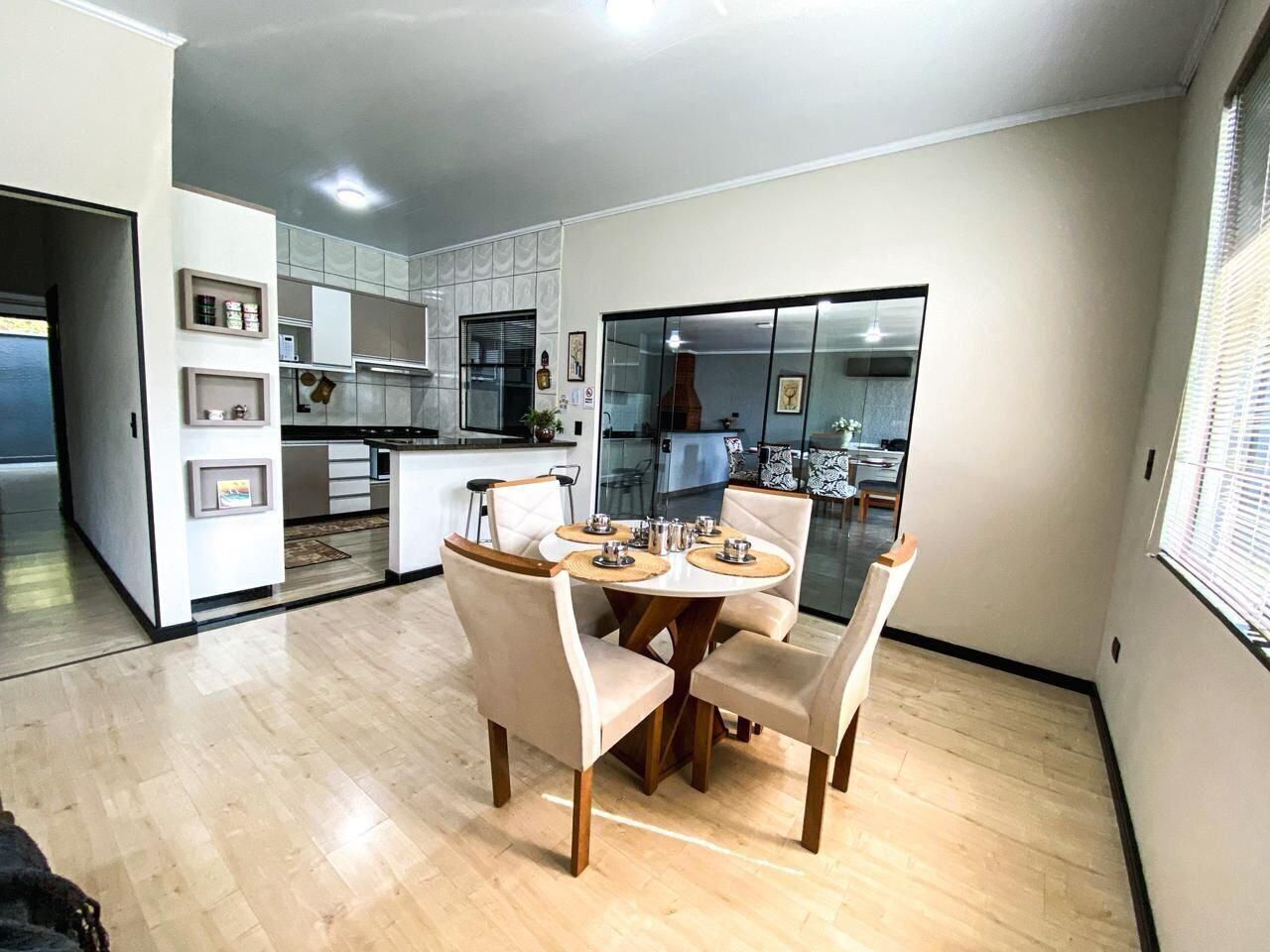 A modern kitchen with white cabinets, a dining area with a round table and chairs, and a large window.