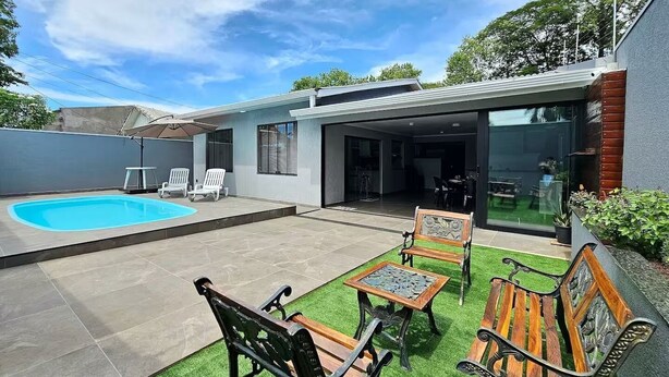 Una casa moderna con piscina, mobiliario de patio y un área exterior techada.