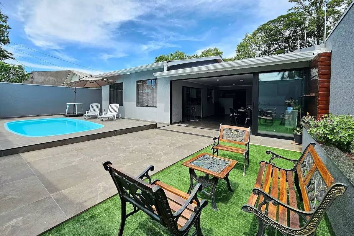 Una casa moderna con piscina, mobiliario de patio y un área exterior techada.