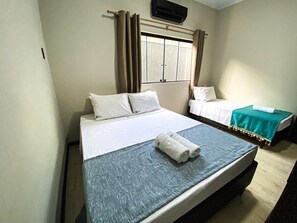 Une chambre d’hôtel avec deux lits, une fenêtre avec des rideaux, un téléviseur à écran plat et une petite table recouverte d’une nappe verte.